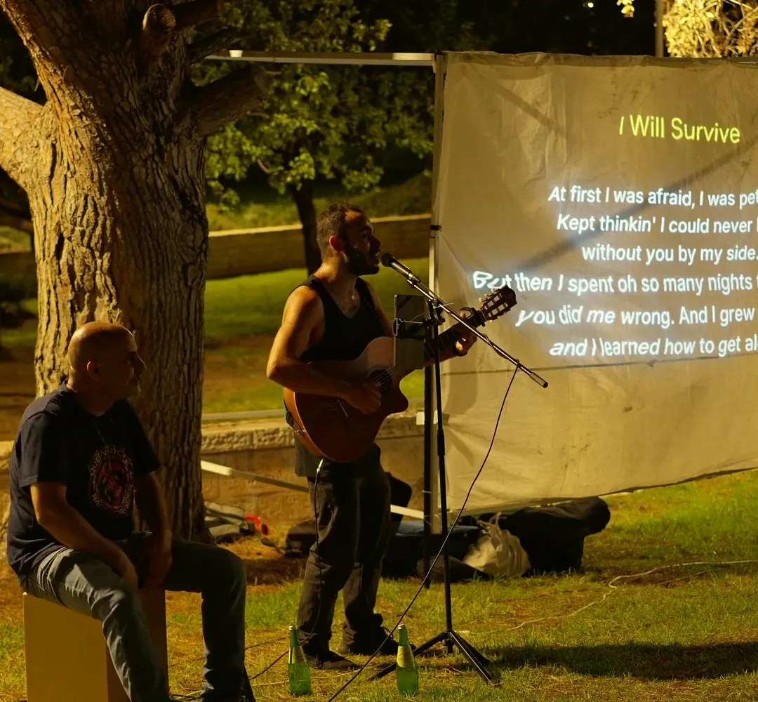 אלון שר ומנגן בגיטרה ליד מסך עם מילות השיר